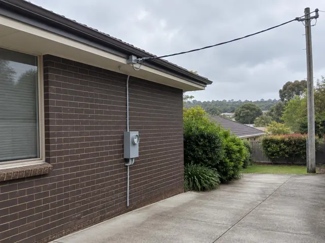 Exterior brick wall with overhead service cable and point-of-attachment bracket on the eaves in Belrose